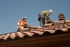 Two roofers install clay tiles on a roof