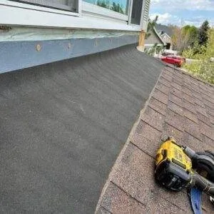 Close-up view of a sloped roof with new shingles, flashing installation, and repair tools, highlighting how roof pitch can impact roof replacement cost. Image taken during a residential roofing project in Denver by Elite Roofing & Solar.