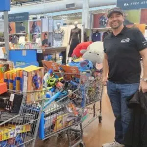 Cody Hayes of Elite Roofing & Solar inside a store beside carts full of toys for the 10th Annual Toys for Tots drive in Denver
